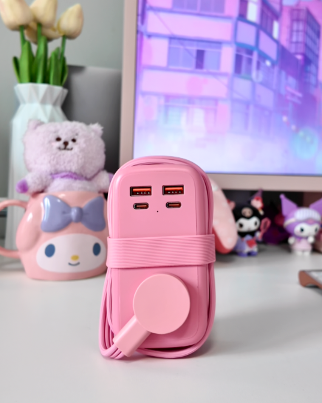 A close up shot of the pink NTONPOWER GaN 65W travel power strip with its cord neatly wrapped around the base, styled on a clean white desktop next to a cute pastel purple plush toy in a My Melody mug.