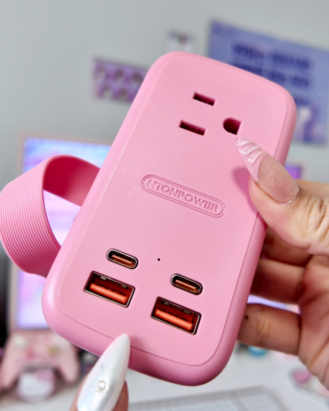 A close up of a hand holding a pastel pink NTONPOWER power strip, clearly showcasing its two USB A ports, two USB C ports, and top AC outlet against a soft, blurred background.
