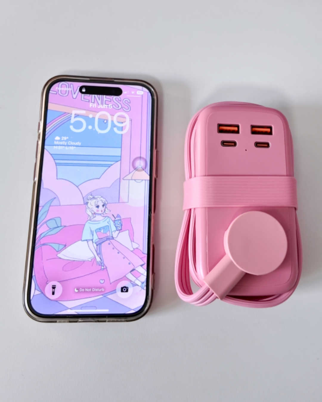 A flat lay size comparison showing a compact, neatly wrapped pink NTONPOWER travel power strip sitting side by side with an iPhone displaying an anime lock screen.