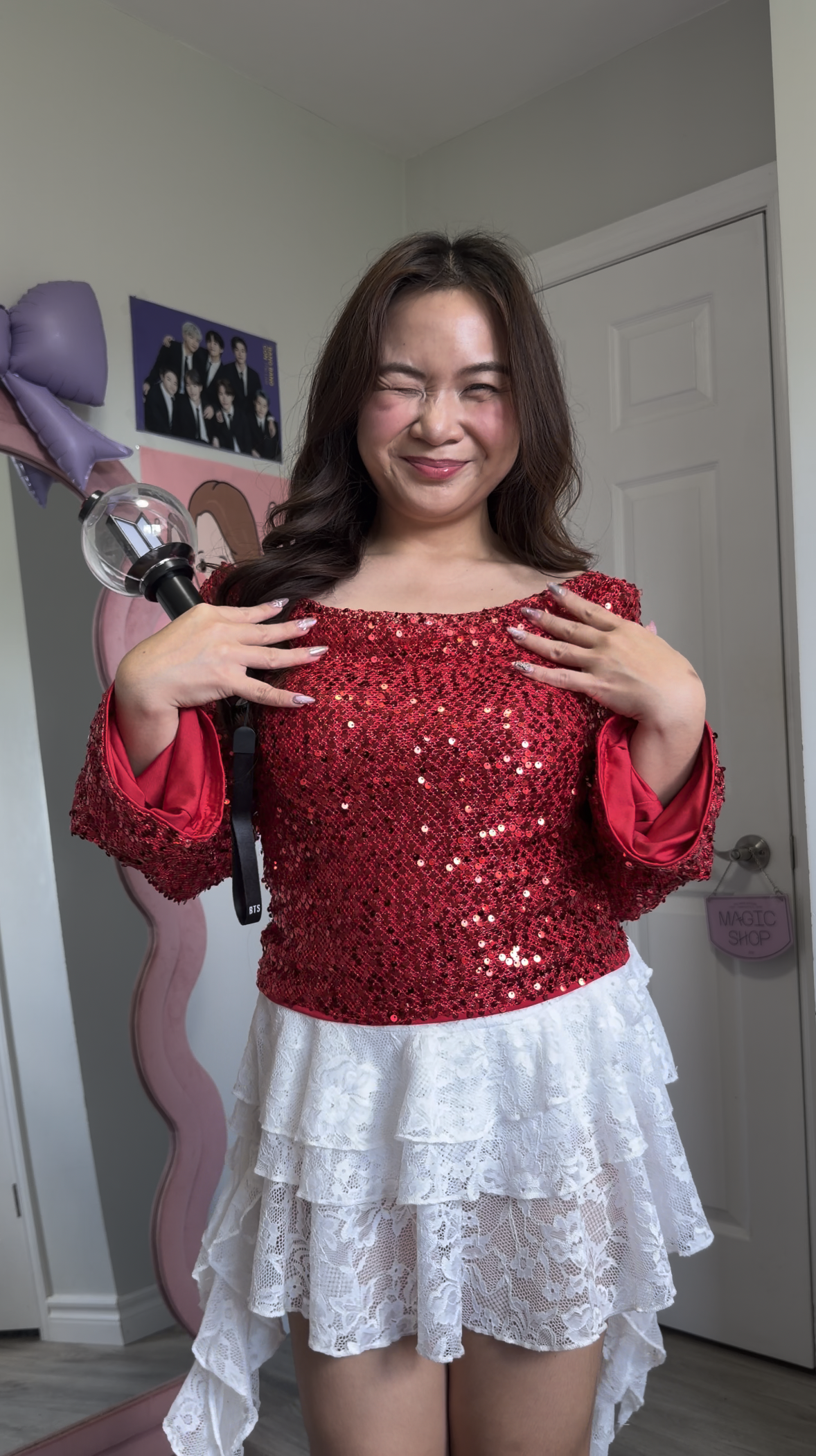 Roxanne a Toronto creator winking while holding an ARMY Bomb lightstick wearing an off the shoulder bright red sequin bell sleeve top.