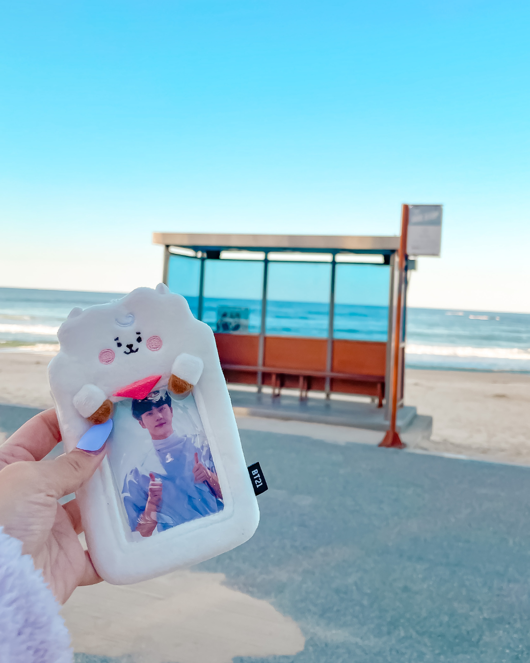 TS Jin photocard in RJ BT21 holder held up at the Spring Day bus stop at Hyangho Beach Gangneung Korea