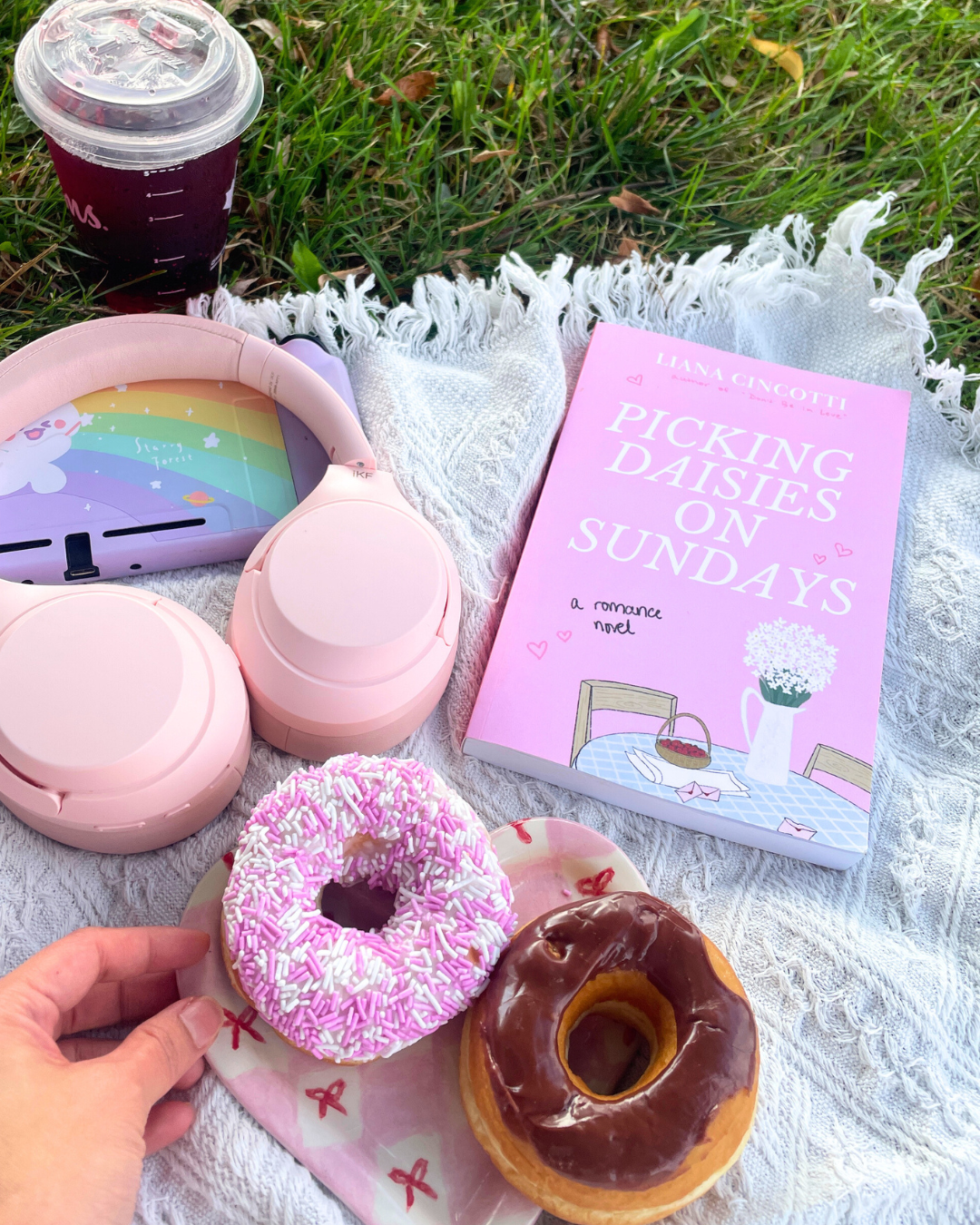 cute spring picnic flatlay with a pink romance novel pink headphones donuts and an iced drink on a blanket whimsy spring activities Toronto lifestyle content creator