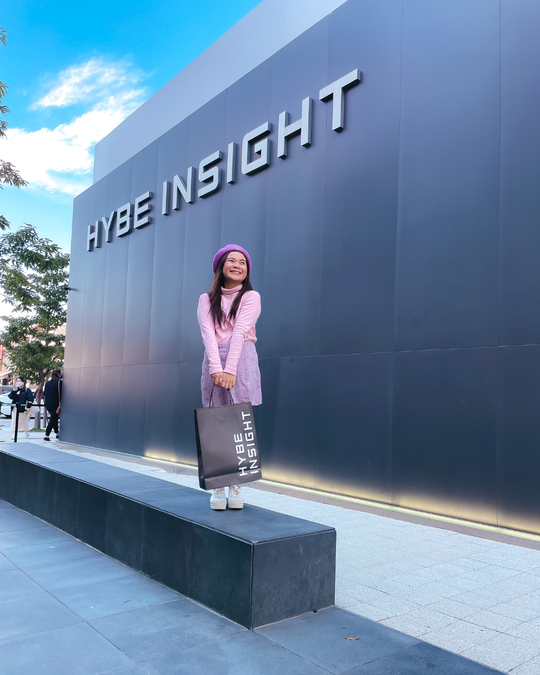 Roxanne Lacap in a purple outfit standing in front of the HYBE Insight sign in Seoul Korea