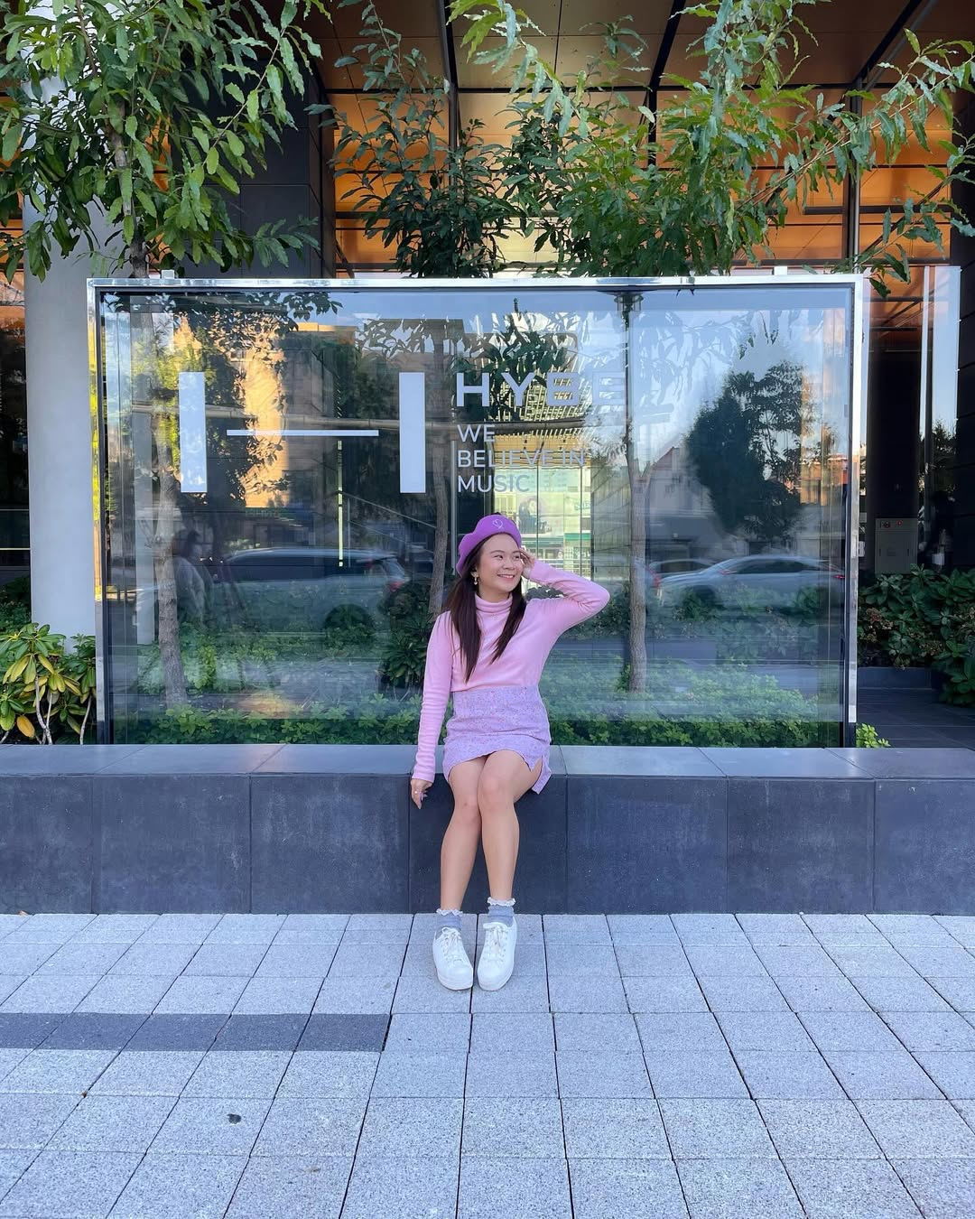 Roxanne Lacap a BTS ARMY sitting in front of the HYBE headquarters We Believe in Music sign in Seoul Korea