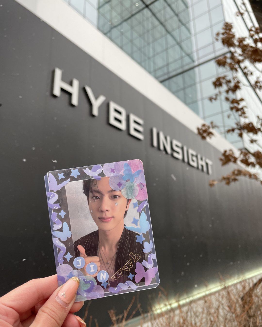 Jin BTS photocard held up in front of the HYBE Insight sign in Seoul Korea