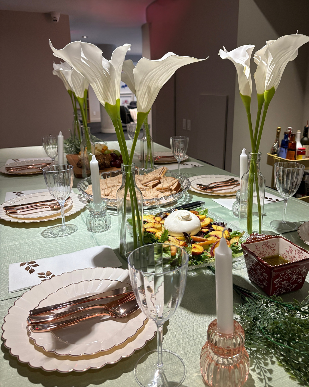 elegant spring dinner party table with tall white calla lilies rose gold cutlery scalloped plates candles and a burrata peach salad whimsy spring activities
