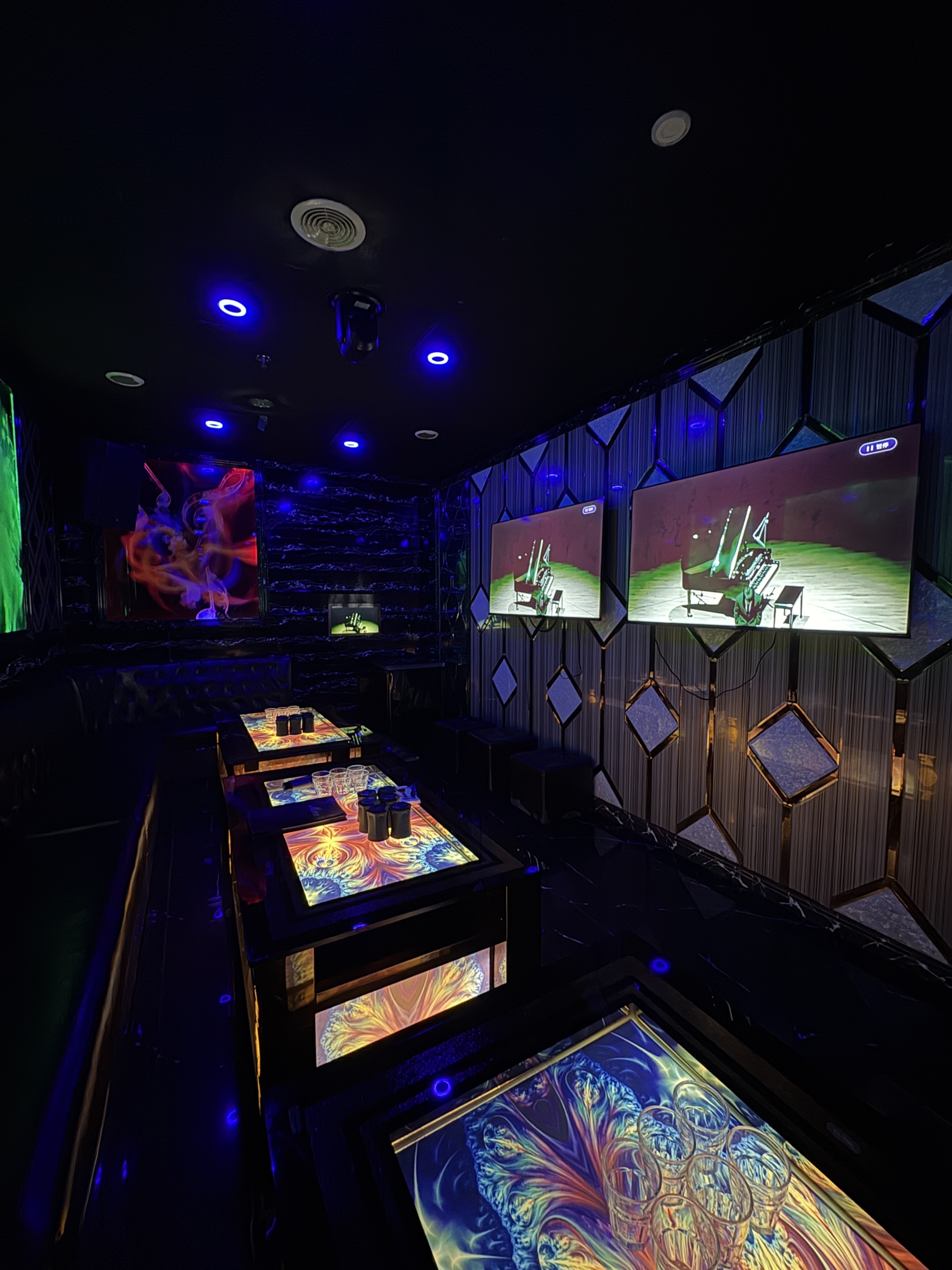 A wide angle view of the interiors of a luxury private karaoke lounge at ET KTV Markham featuring interactive light up tables and multiple large screens playing music videos.