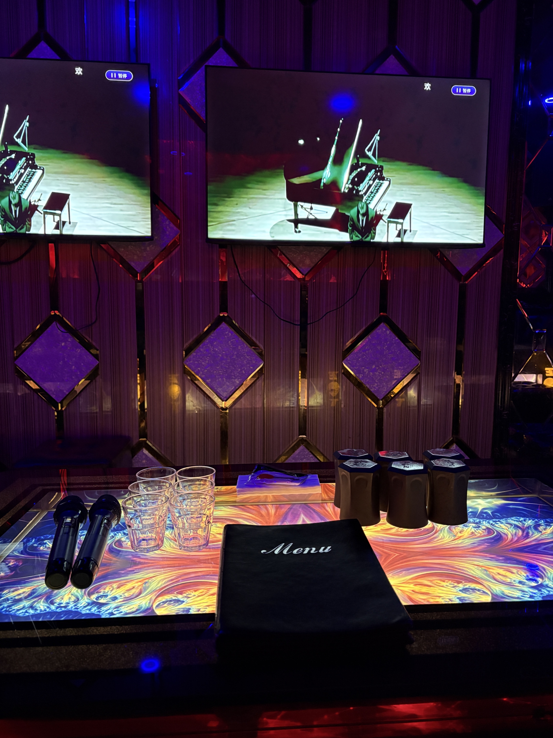 A close up view of a private KTV table setup at ET KTV Markham with two microphones, glasses, a food menu, and dual wall mounted screens.