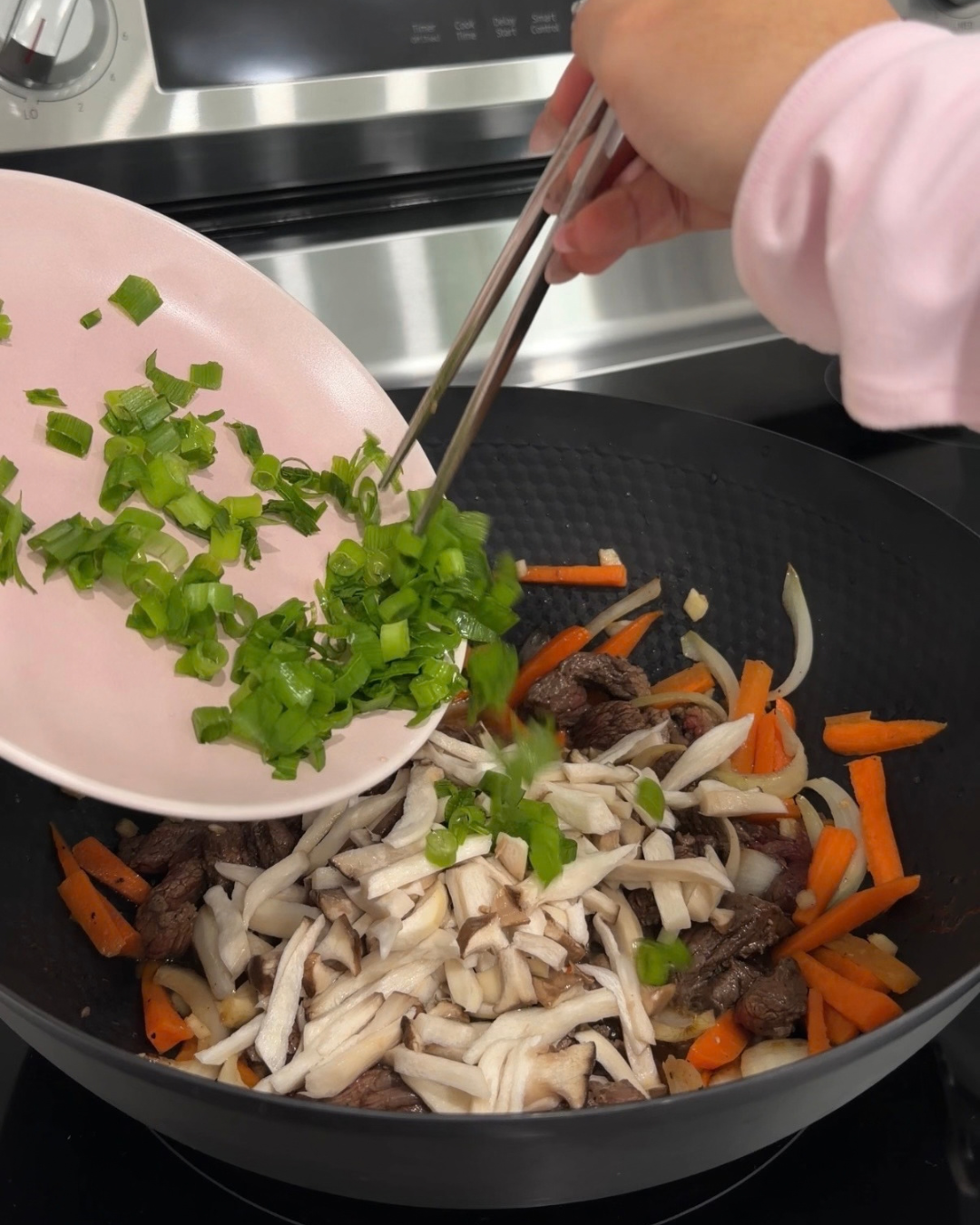 Stir-frying green onions, oyster mushrooms, carrots, and beef inside a Cooker King 32cm wok on the stove
